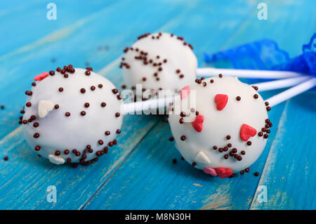 Holiday treats. Cake pops. Biscuit cakes in white chocolate glaze on a bright blue wooden background. Stock Photo