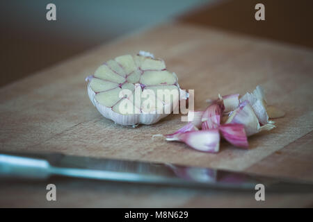 Raw garlic (Allium sativum) being chopped on a wooden chopping board Stock Photo