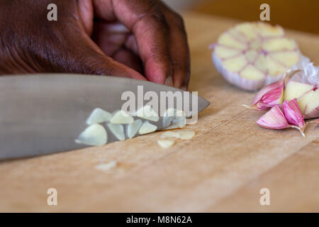 Raw garlic (Allium sativum) being chopped on a wooden chopping board Stock Photo