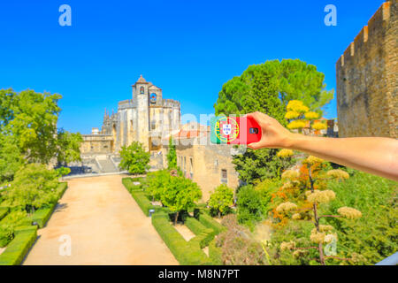 Tourism and travel concept in Europe.Mobile phone with Portugal flag cover taking photos of tourist attractions in city of Knights Templar. Church of Convent of Christ on blurred background.Copy space Stock Photo