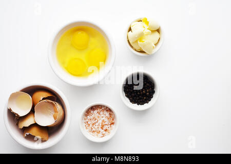 Three organic brown eggs in white bowl on white background. Used eggs shells in second bowl and shot top down. Pink salt and black pepper corns. Stock Photo