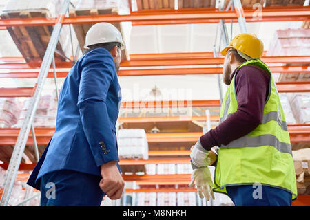 Back view low angle portrait of warehouse manager and factory worker looking up at tall storage shelves in warehouse Stock Photo