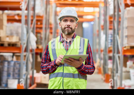 Waist up portrait of mature warehouse worker using digital tablet looking at camera, copy space Stock Photo