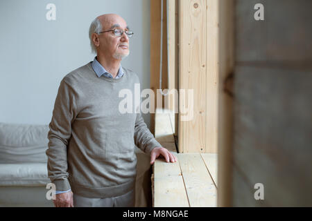 Pensive senior man looking through window Stock Photo