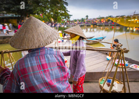 Vietnam women, two female vendors wearing Vietnamese conical hats chat along the waterfront in Hoi An, Central Coast, Vietnam.