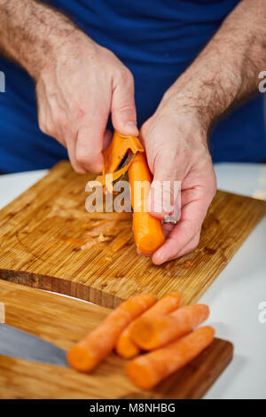 Man peeling carrots on a wooden board Stock Photo