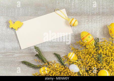 Easter accessories, mimosa and yellow daffodils on a light wooden surface. Yellow orange easter concept, top view, copy space with postcard for writin Stock Photo