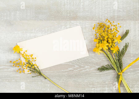 Mimosa and yellow daffodils on a light wooden surface. Yellow orange flowers concept, top view, copy space, postcard for writing on a wooden surface Stock Photo