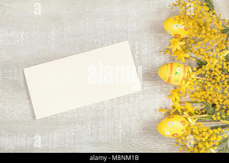 Composition with painted eggs. Easter accessories, mimosa and yellow daffodils on a light wooden surface. Yellow orange easter concept, top view, copy Stock Photo