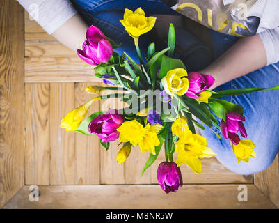 Young woman sits on a wooden floor with a colorful bouquet of spring flowers. Stock Photo