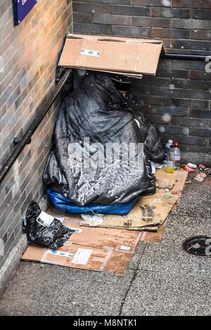 Homeless man huddled in corner of underpass with snow on bedding. Homelessness. Snowing. Freezing. Sleeping rough in winter. London, UK Stock Photo