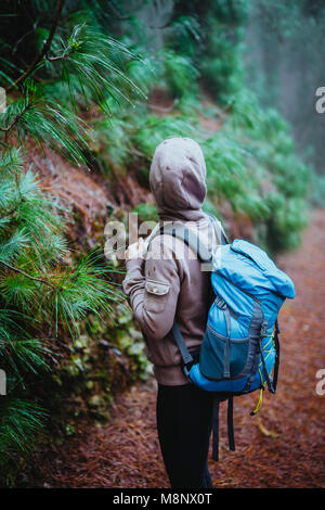 Female traveler wearing hood on the road in the mysterious foggy pine forest. Santo Antao Island, Cape Verde Stock Photo