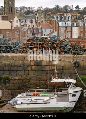 North Berwick, East Lothian, Scotland, United Kingdom,  Boat stranded in harbour at low tide with lobster creels on pier. Seaside houses in background Stock Photo