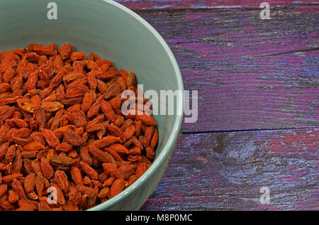 Ceramic bowl full of dry Goji berries on old wooden background in vintage style.Close , flat, horizontal view from above. Stock Photo