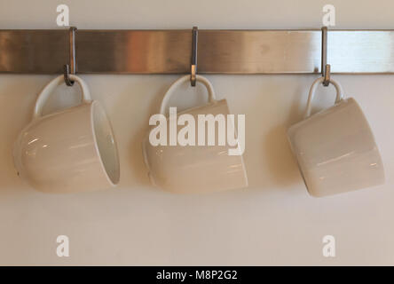 Three white mugs haning on wall Stock Photo