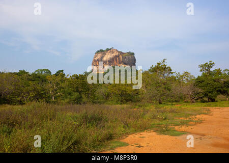 sigiriya rock formation in rural sri lanka with tropical forest and sandy track under a blue sky Stock Photo