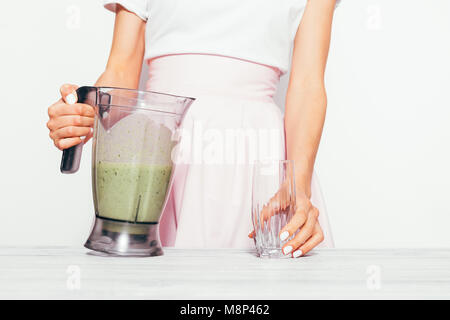 Slender young woman in a pink skirt pours a green smoothie from a banana and spinach into a glass Stock Photo