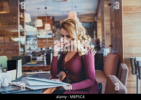 Pretty Woman sitting in Restaurant and Reading Menu. Perfect Redhead Girl in Cafe Stock Photo