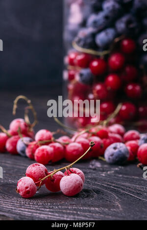 The frozen red currant in the hoarfrost lies on the wooden olympic table against the background of other berries and a glass bulb Stock Photo
