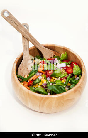 Pasta salad in a wooden bowl, with sweetcorn, onion, tomatoes and spinach. and with salad serving utensils. Stock Photo