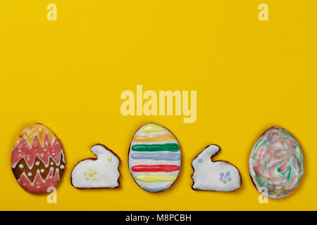 Homemade cookies in the form of Easter eggs and rabbits on a yellow background with space for text, top view Stock Photo