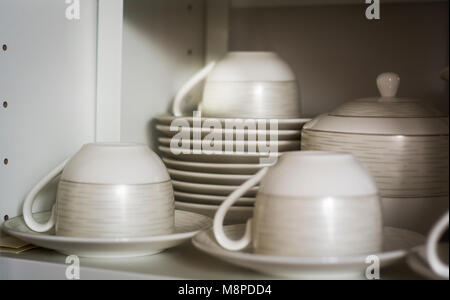 decorated coffee cups and saucers on the shelf of a white pantry Stock Photo