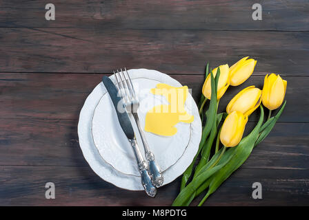 Place Setting for Easter, olored easter eggs and  bouquet of yellow tulips on a wooden background Stock Photo