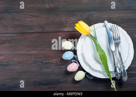 Place Setting for Easter, olored easter eggs and  bouquet of yellow tulips on a wooden background Stock Photo
