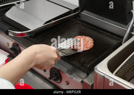 Cook frying cutlet on grill and turning over the cutlet for burger Stock Photo