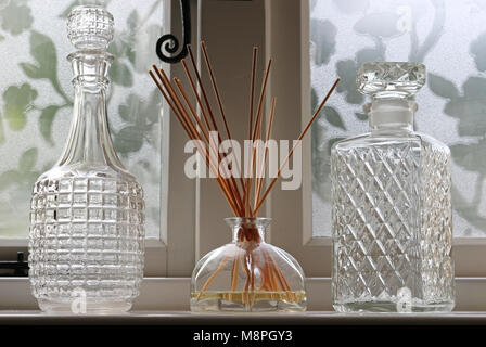 A Reed Diffuser on a windowsill between two decanters Stock Photo