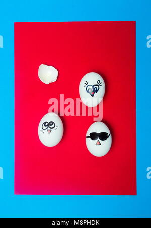 White eggs with drawn faces on red background top view Stock Photo