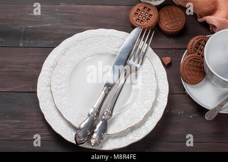 Empty white plates with silverware  knife and fork , cup ,jug and chocolate cookies  on dark wooden table background. Table setting. plate fork knife  Stock Photo