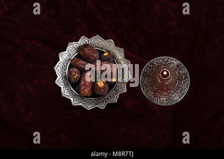 Close-up portrait of dates which are a traditional food to break fast during the holy month of ramadan on a silver serving platter on a red cloth. Dub Stock Photo