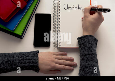 Womans hand writing word update in a notebook on a desk. Project update checklist. Notebook, pen and books. System update Stock Photo