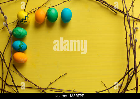 Colorful Easter eggs on yellow wooden background, in twigs frame. Easter greeting card. Happy Easter concept Stock Photo