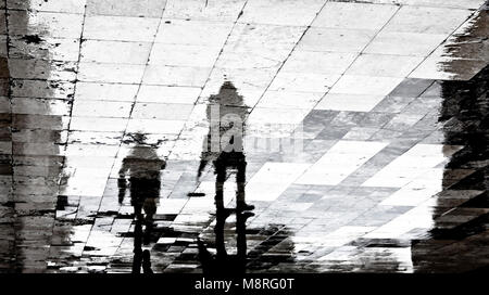 Blurry reflection shadow silhouette of two people walking  the city street patterned sidewalk on a dark rainy day Stock Photo