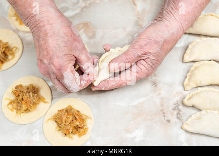 Hands of the old woman mold vareniki with cabbage over the table Stock Photo
