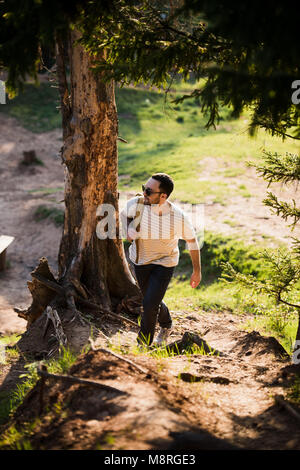 Happy bearded man traveler with backpack walking in forest. Tourism, travel, adventure, hike concept - smiling young man walking with backpack in woods. Concept of clean air and healthy lifestyle. Stock Photo