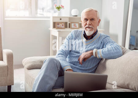 Charming senior man posing while using laptop on couch Stock Photo