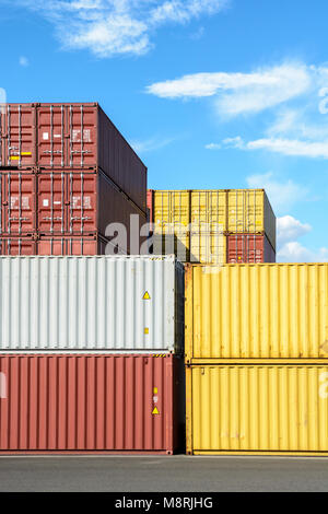 Dry cargo containers of different colors stacked in a shipping yard under a blue sky with white clouds. Stock Photo