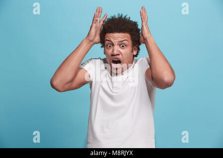 The young emotional angry man screaming on blue studio background Stock Photo