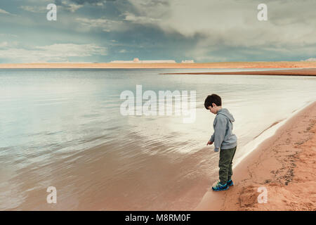 Side view of boy standing by Lake Powell against cloudy sky Stock Photo
