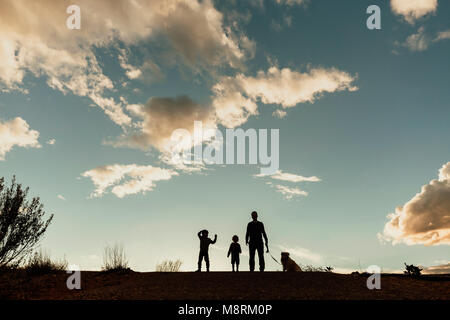 Silhouette father with sons and dog standing on field against cloudy sky during sunset Stock Photo