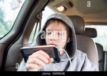 Boy wearing hooded shirt using smart phone while sitting in car Stock Photo