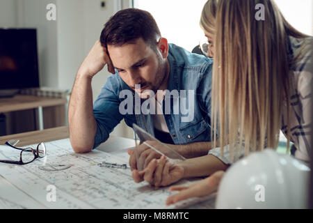 Young worried architect colleagues analyzing blueprints while working on a new project at the office. Stock Photo