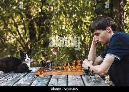 Side view of serious man looking at chess pieces by cat on wooden table at backyard Stock Photo