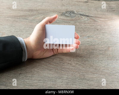 Closeup man hand holding plastic credit card isolated on dark wooden background Stock Photo