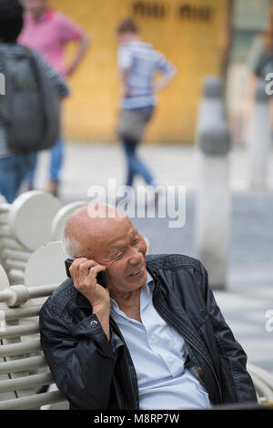 Senior man talking on a mobile phone while seated on a bench in the city of Shanghai, China Stock Photo