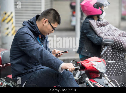 Man checking his mobile phone while sitting on a scooter in Shanghai, China Stock Photo