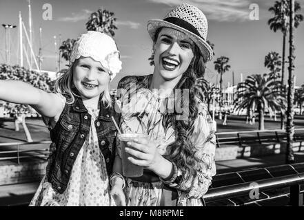 Summertime at colorful Barcelona. smiling elegant mother and daughter travellers in Barcelona, Spain with bright red beverage taking selfie Stock Photo